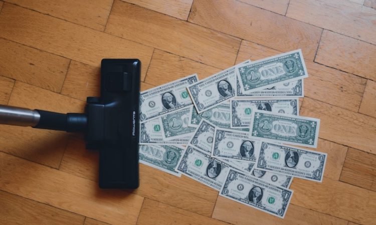 A vacuum cleaner approaching dollar bills on wooden flooring